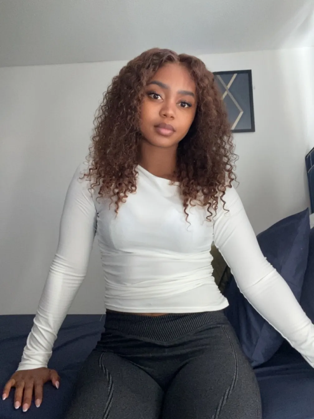 Chloe, Deep Tissue Therapist, white top seated on bed curly hair portrait at All Queens Wellness Spa, Kindaruma Road, Kilimani, Nairobi.